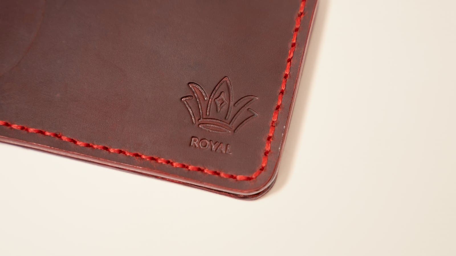 Close-up of burgundy ROYAL leather with red stitching and the embossed crown logo