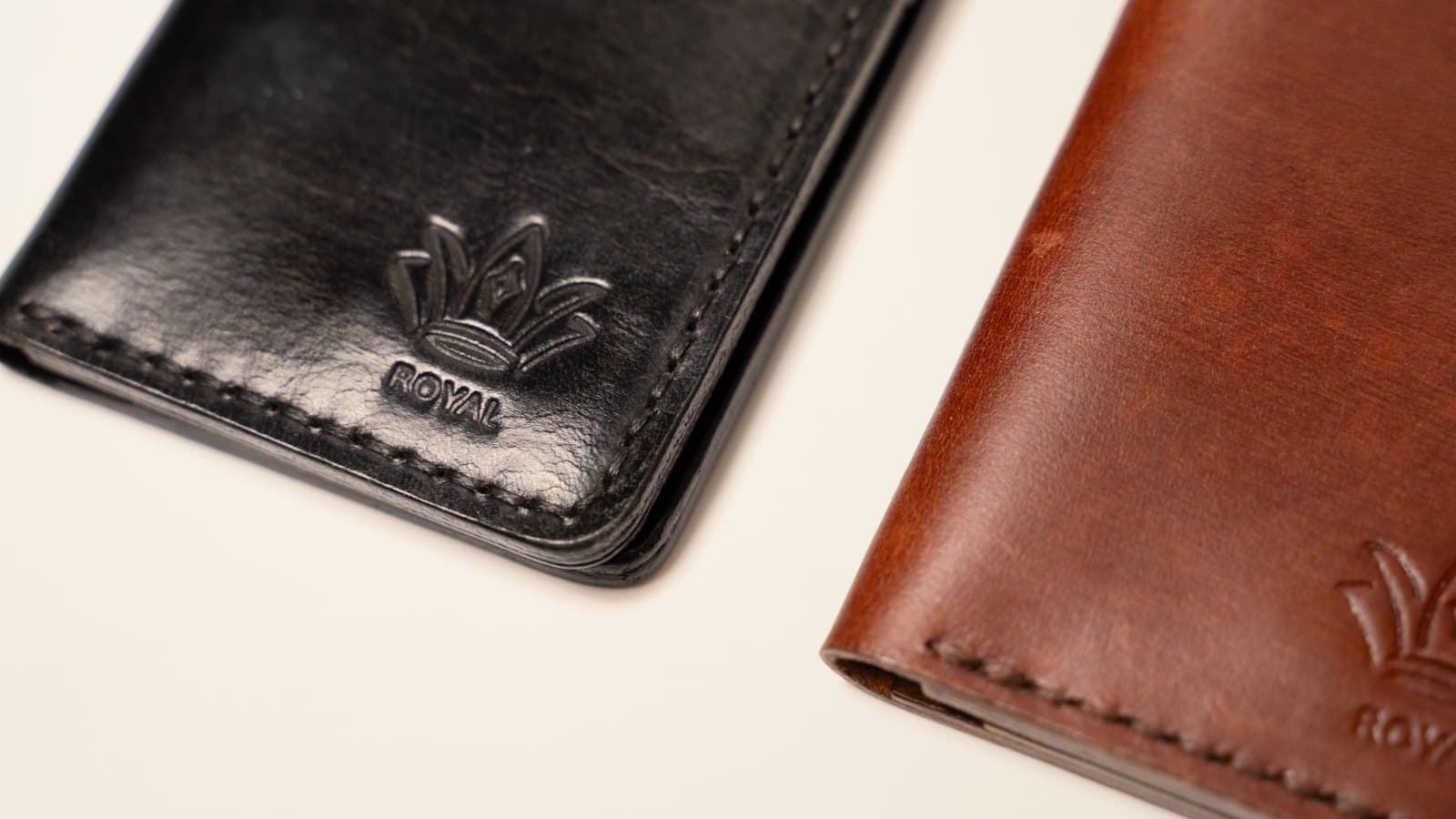 Close-up of two ROYAL leather pieces, black and brown, with the embossed crown logo and stitched edges