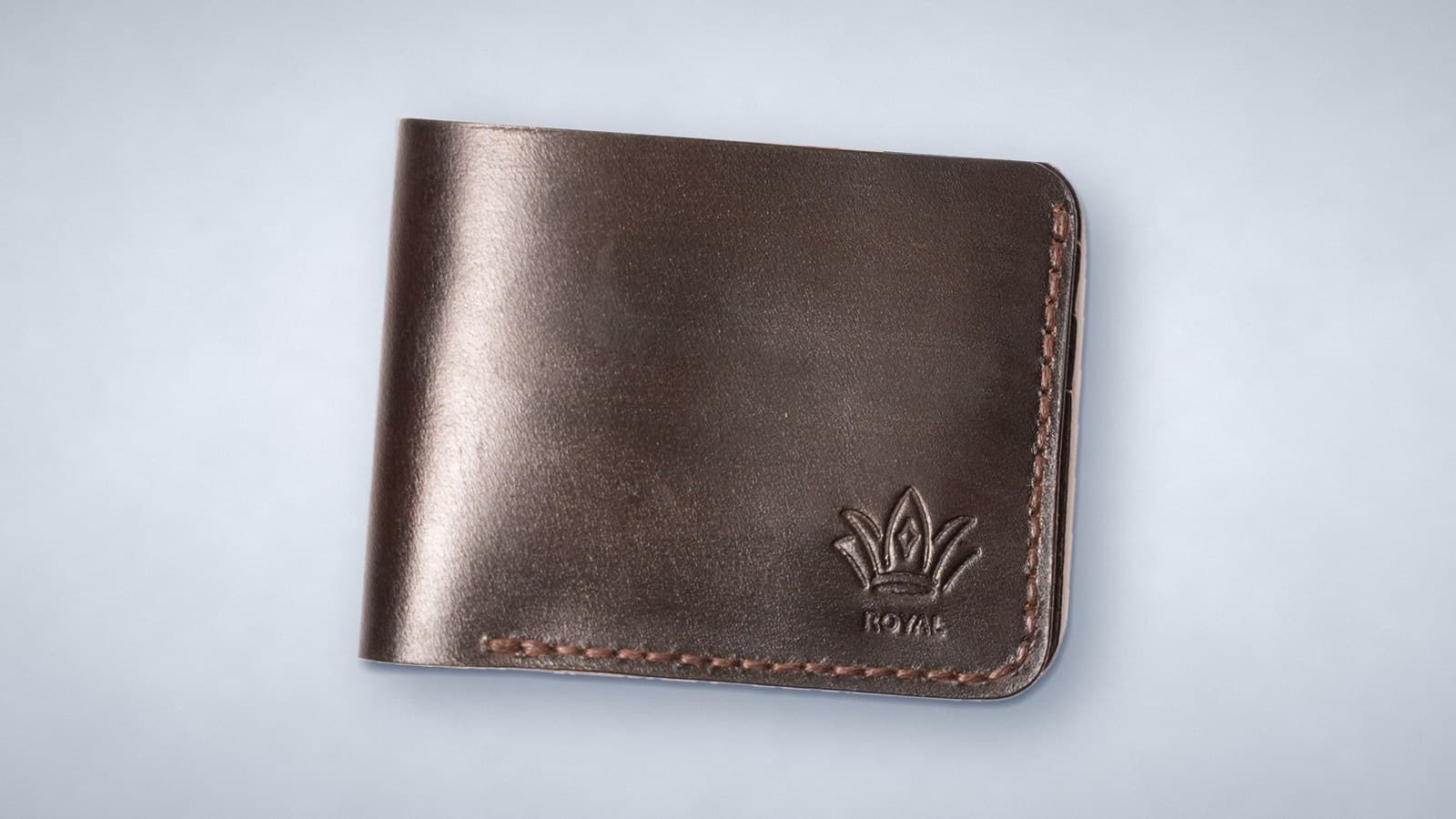 A dark brown ROYAL leather bifold wallet with brown stitching and the embossed crown logo