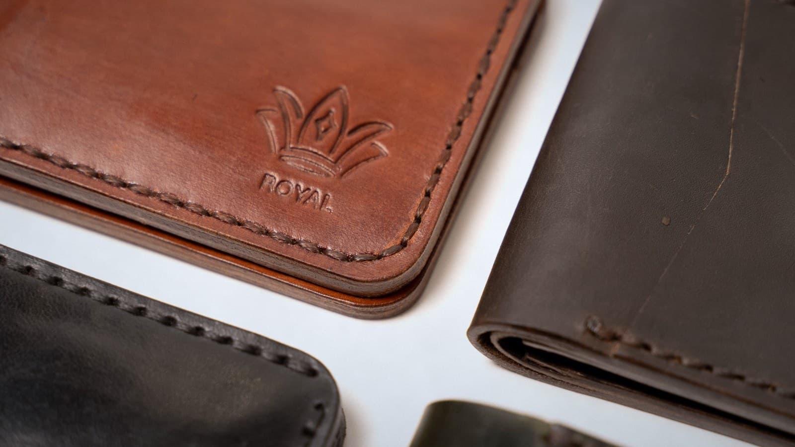 Close-up of ROYAL leather wallets in cognac, black and dark brown, with the embossed crown logo and stitching