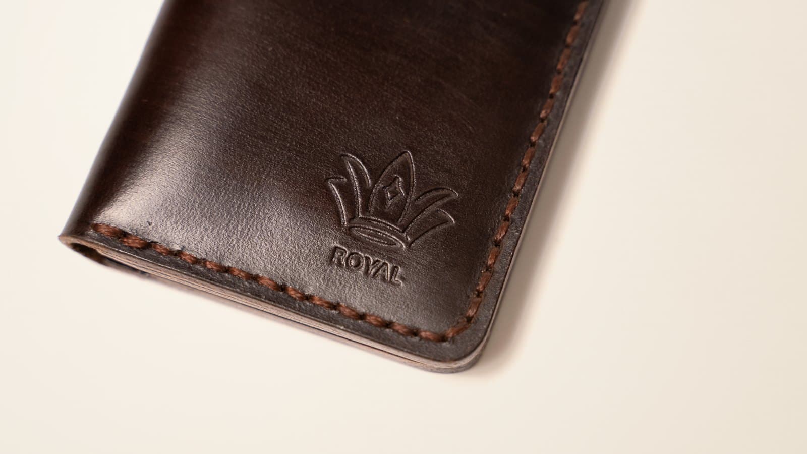 Close-up of the stitched edge and embossed crown logo on a dark ROYAL leather wallet