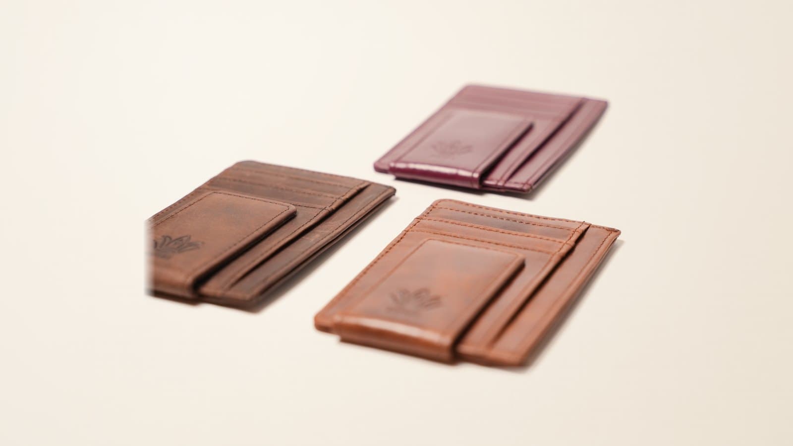 Three slim ROYAL front pocket wallets in burgundy, brown and tan, laid at an angle on an ivory linen backdrop