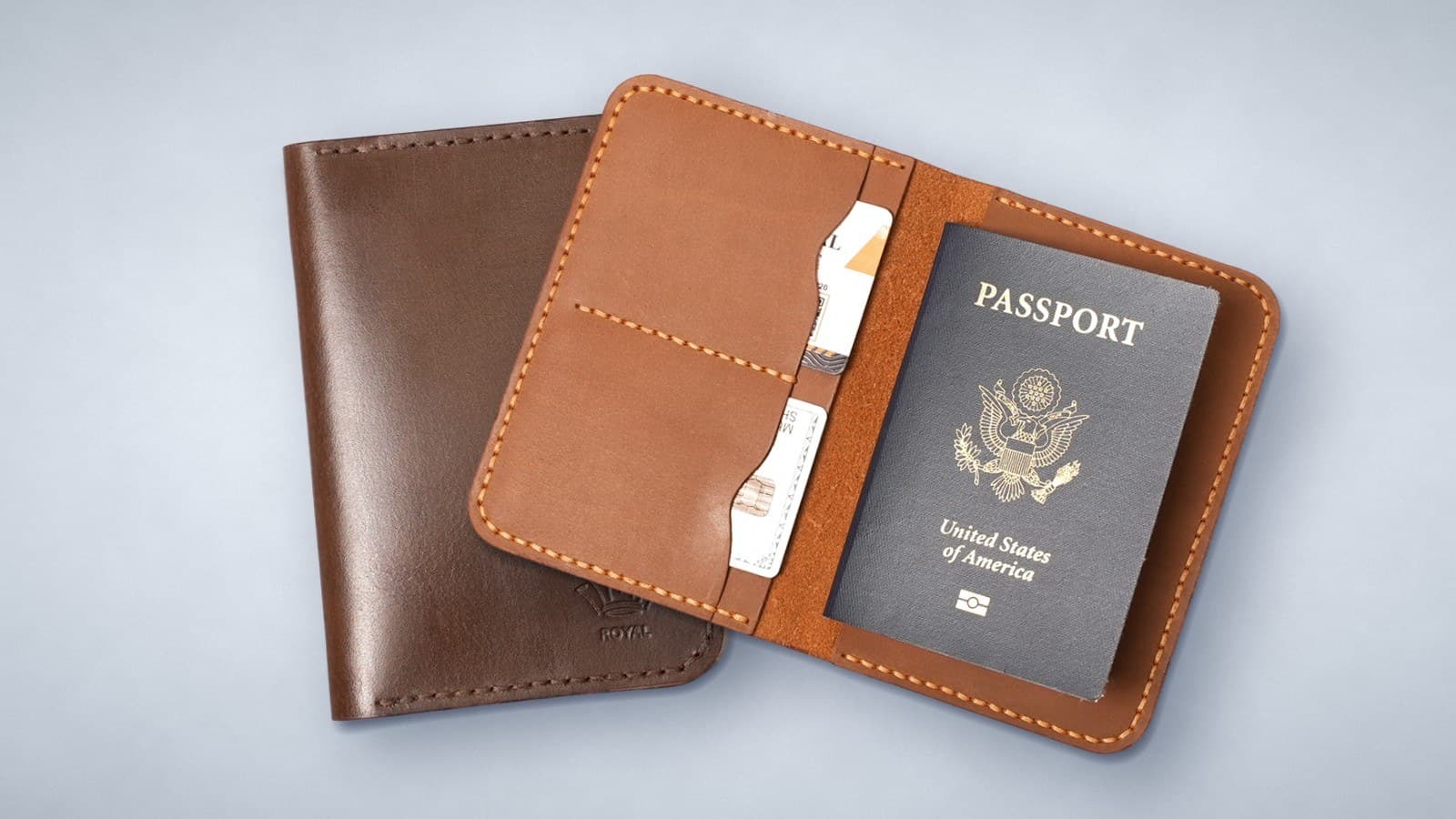 Two ROYAL leather passport covers: a dark brown one closed and a tan one open with a passport and cards