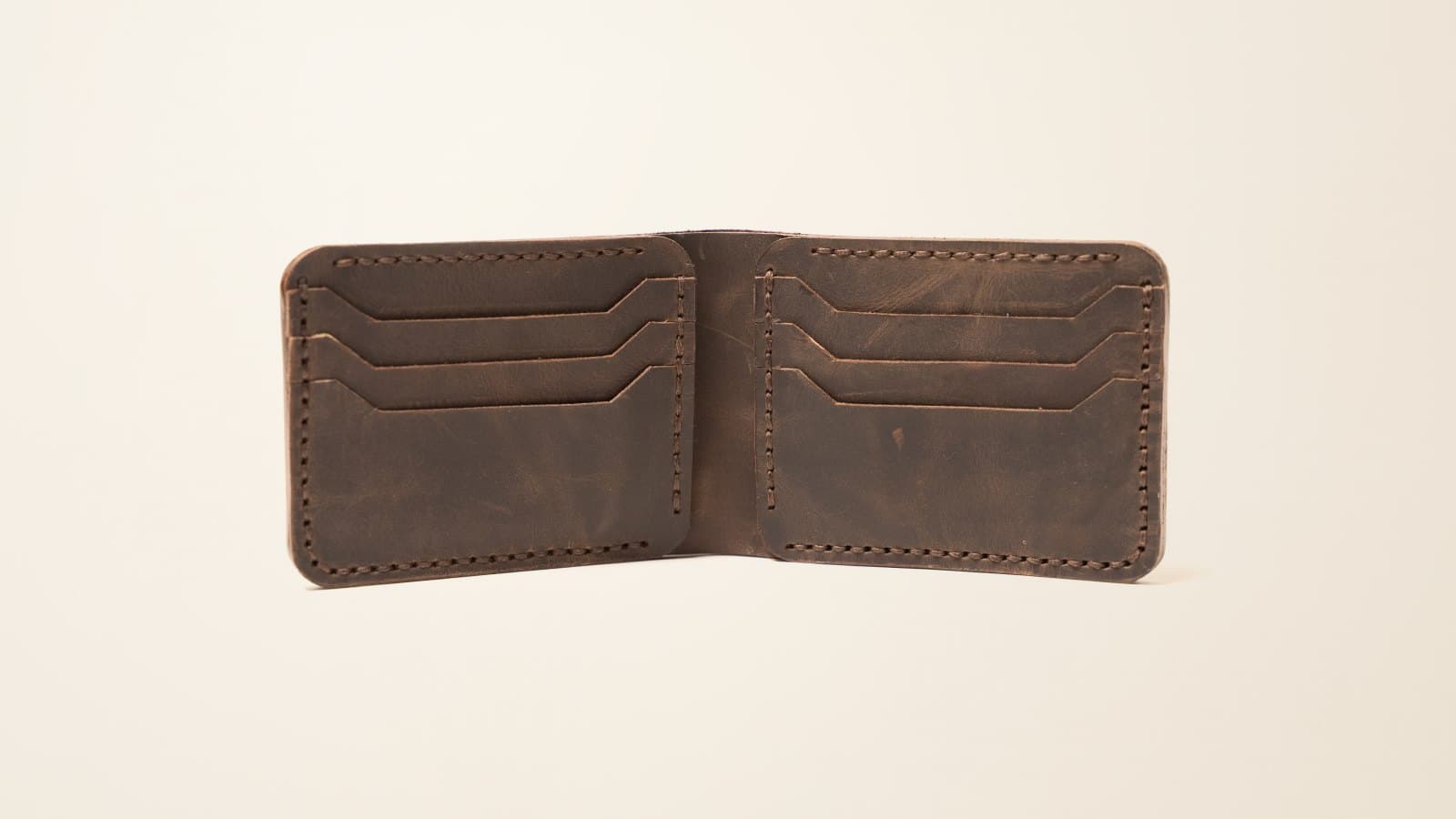 An open brown ROYAL leather bifold wallet showing its card slots, on an ivory linen backdrop