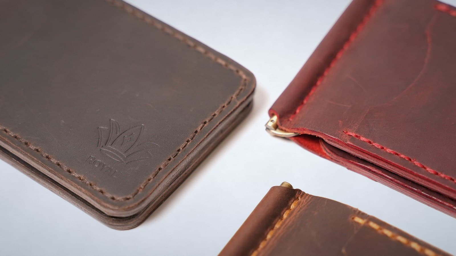 Close-up of the saddle-stitched edges of three ROYAL leather wallets, sewn in brown, red and tan thread