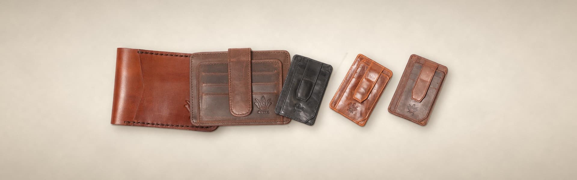 ROYAL bestsellers on a warm cream surface: a cognac front pocket wallet, a brown signature card holder and magnetic card holders in cognac, black and blue