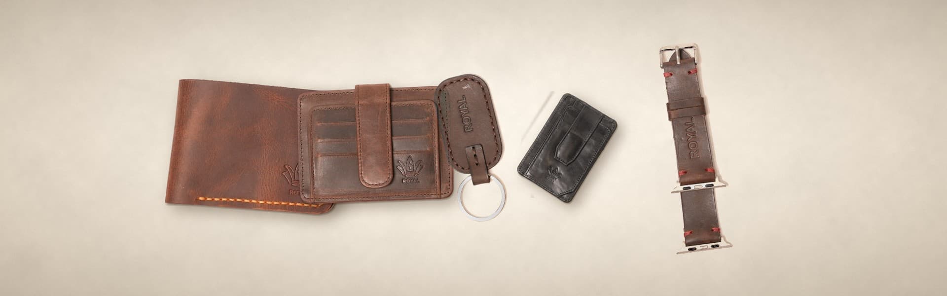 ROYAL everyday carry on a warm cream surface: a tan wallet, a brown card holder, a brown keychain, a black magnetic card holder and a brown watch strap