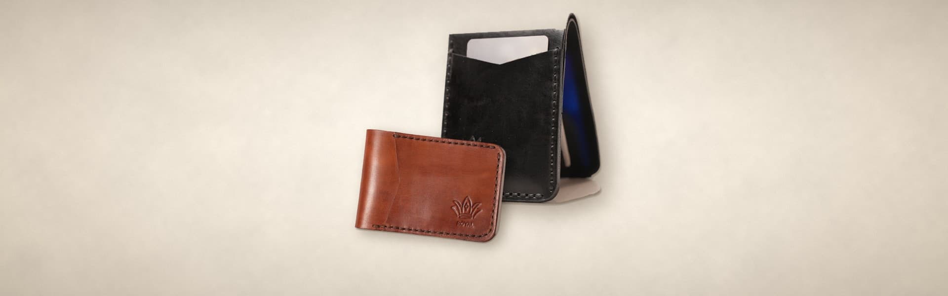 ROYAL front pocket wallets: a black slim bifold standing with a card in its outside slot and a cognac one closed in front, on a warm cream surface