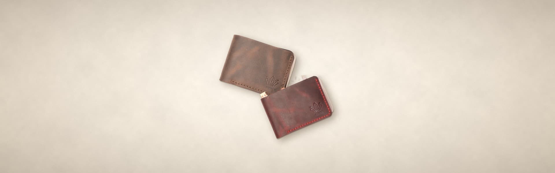 ROYAL hidden pocket bifold wallets in chocolate and burgundy, the burgundy one open to show the hidden cash pocket, on a warm cream surface