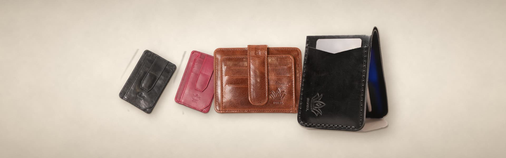 ROYAL minimalist carry on a warm cream surface: magnetic card holders in cognac, dark brown and burgundy, a cognac signature card holder and a black front pocket wallet