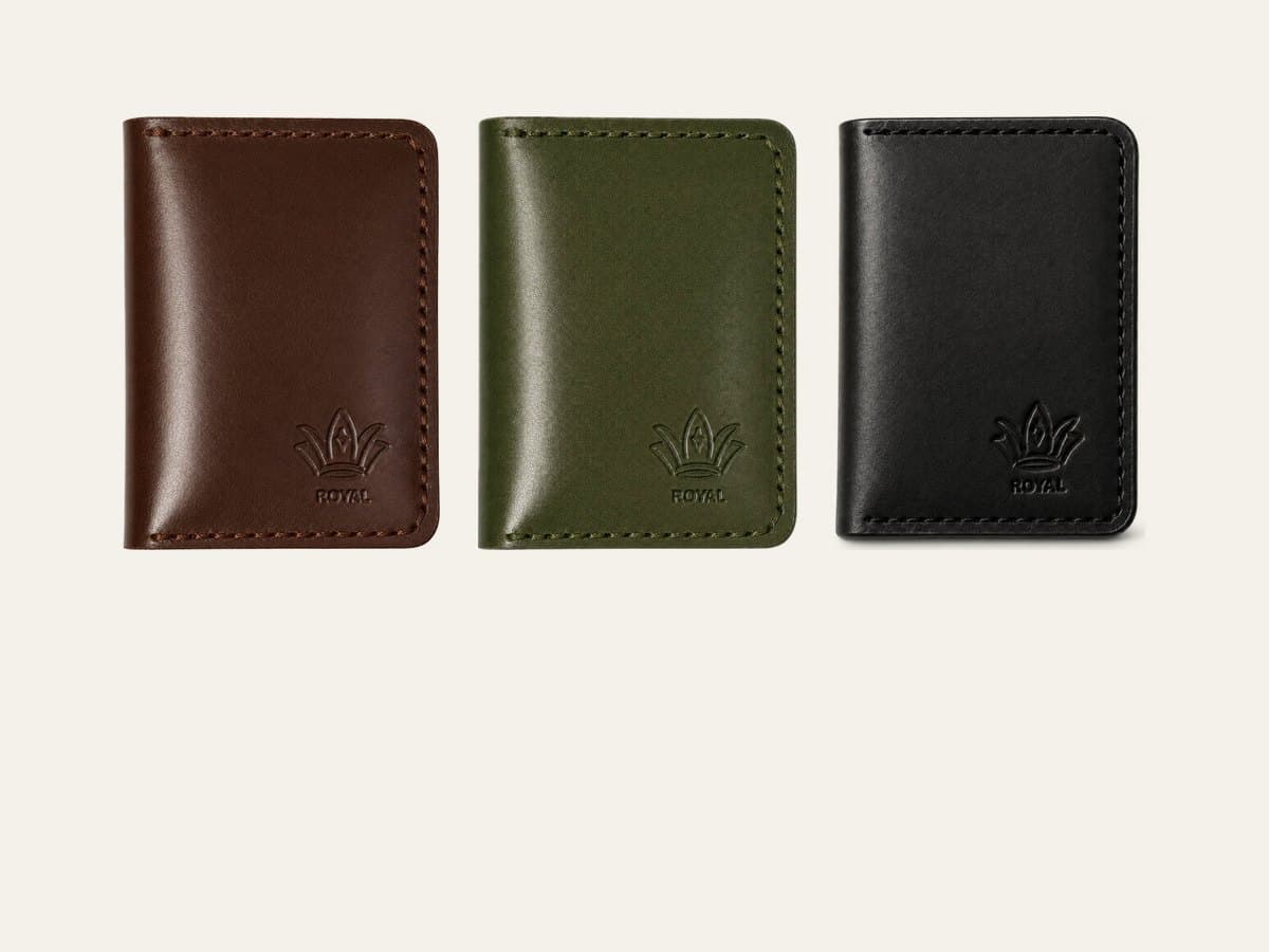Three ROYAL leather card holders in dark brown, burgundy and cognac on a warm cream surface