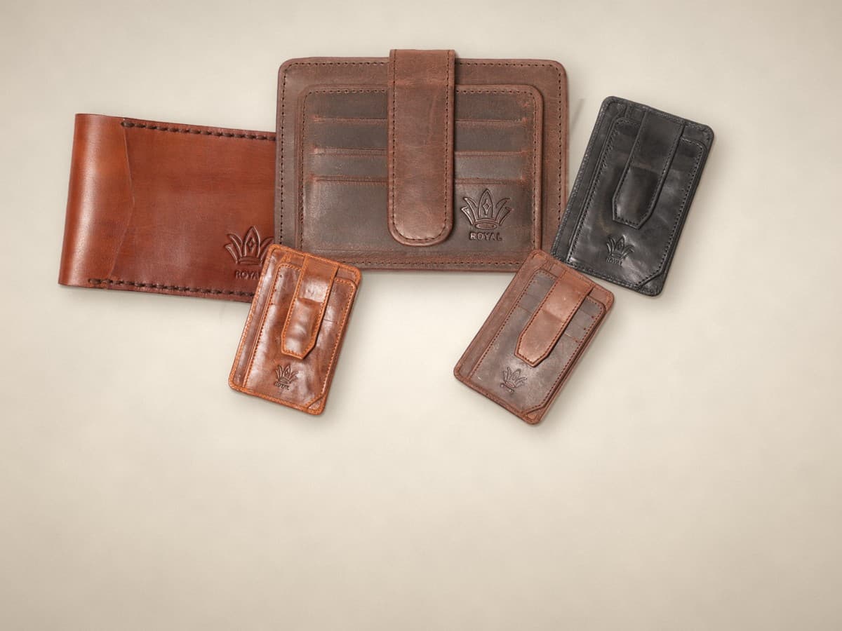 ROYAL bestsellers on a warm cream surface: a cognac front pocket wallet, a brown signature card holder and magnetic card holders in cognac, black and blue