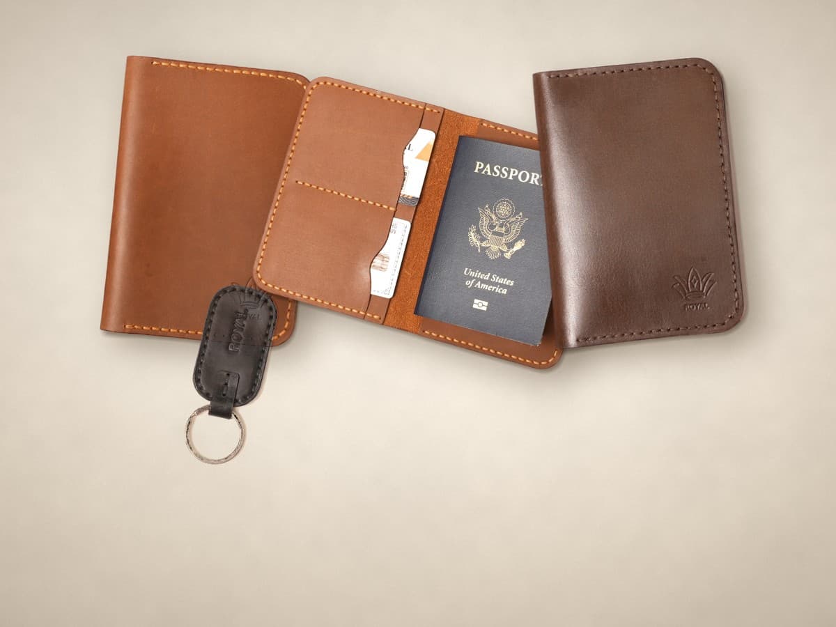 ROYAL leather passport covers in tan and dark brown, an open cover holding a passport and a black keychain on a warm cream surface