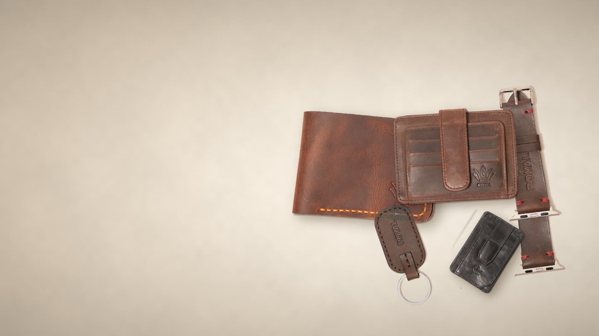 ROYAL everyday carry laid out on a warm cream surface: a tan leather wallet, a brown card holder, a brown keychain, a black magnetic card holder and a brown Apple Watch strap