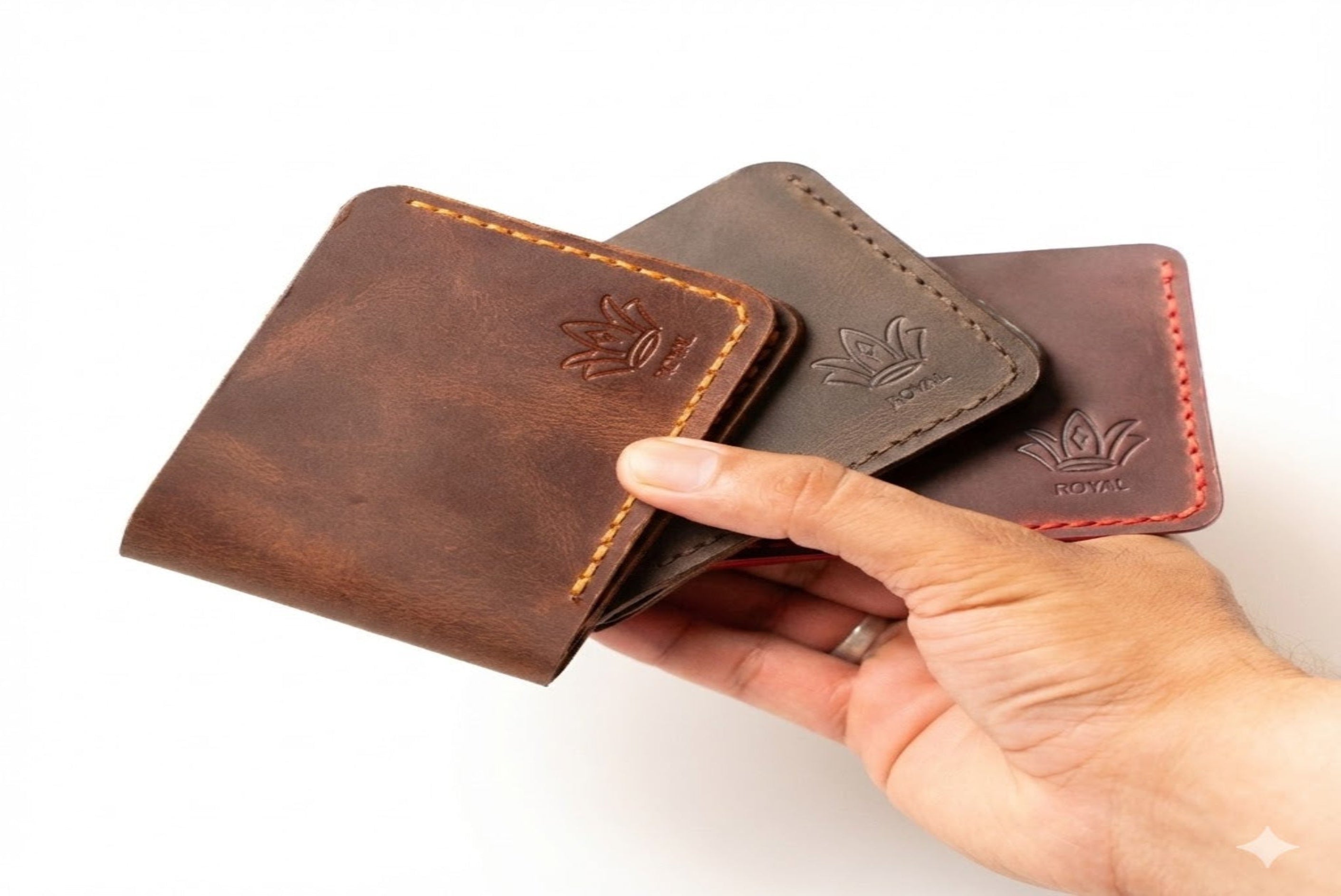 Hand holding three leather wallets with visible brand logo on a white background